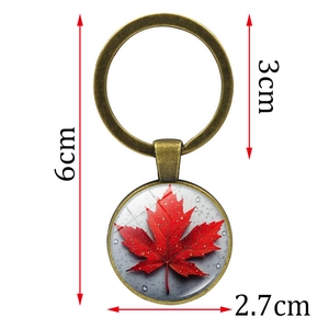 Bronze maple leaf keychain with red pattern and glass dome on a white background