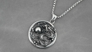 Détail macro du pendentif rond avec dragon en relief et chaîne à mailles carrées en acier