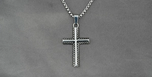 Detailed close-up of a silver titanium steel cross pendant with a box chain on gray texture