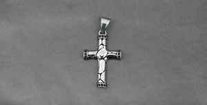 Macro view of a 3D sculpted cross pendant with black micro-stones on dark fabric