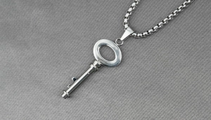 Dettaglio del ciondolo a chiave vintage in acciaio argento su tessuto grigio