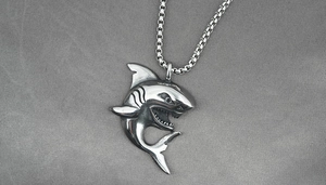 Macro shot of a silver shark pendant with a classic box chain on textured fabric