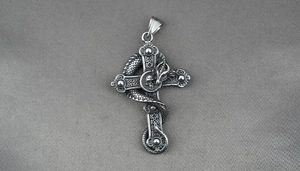 Detailed close-up of a Gothic silver dragon pendant with cross and skull on gray fabric