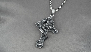 Macro detail of gothic flying dragon cross necklace with snake and skull in vintage steel