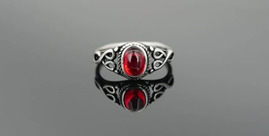 Macro view of vintage titanium steel ring with red oval gemstone and ornate vine patterns