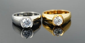 Close-up of polished silver and gold rings with round brilliant-cut zircons on a dark mirror