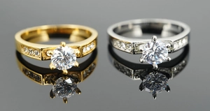 Macro shot of gold and silver six-prong diamond rings on a black reflective surface