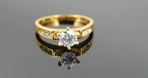 Macro shot of gold-plated ring with a large six-prong set round zircon on black reflective surface