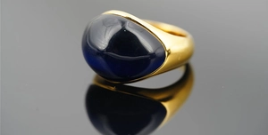 Macro di un anello largo dorato con una grande pietra cabochon blu notte incastonata