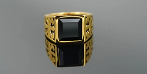 Macro detail of men's gold ring with square black gemstone and hollow cross design