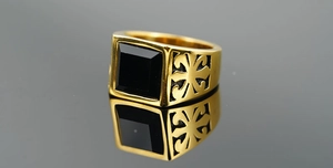 Detailed close-up of golden signet ring with square black stone and hollow side patterns