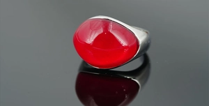 Dettaglio anello a fascia larga in argento con grande gemma rossa ovale su sfondo nero