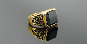 Gros plan de bague dorée pour homme avec pierre noire carrée et détails sculptés