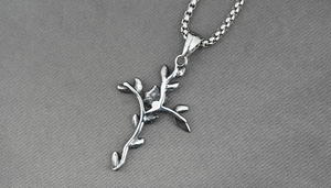 Détail macro du pendentif croix en branche de rose argentée avec textures métalliques fines