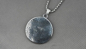Macro shot of silver metal round pendant featuring a dot-matrix texture on the reverse