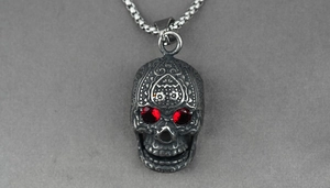 Close-up of gothic stainless steel skull pendant with red gemstone eyes and floral carvings