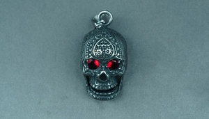Detailed macro view of a vintage skull pendant with red gem eyes and intricate floral carvings