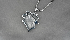 Macro detail of silver rooster head pendant with textured surface and box chain necklace