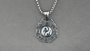 Detail of silver octagonal yin yang pendant with box chain on dark textured fabric