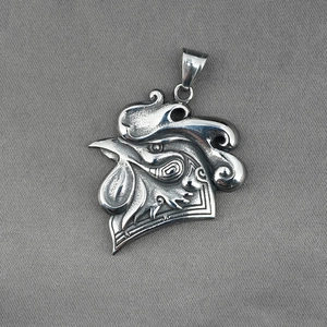 Polished stainless steel rooster head pendant on a textured gray background