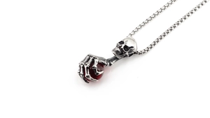 Macro detail of retro skull pendant with skeletal hand clutching a red gem bead