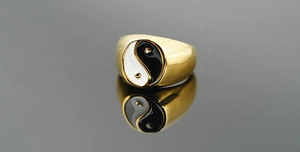 Macro shot of gold-plated Yin Yang ring with black and white enamel on a reflective surface