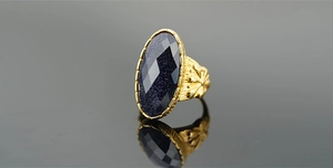 Dettaglio della grande pietra ovale blu sabbia con incisioni floreali sulla montatura