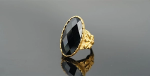 Dettaglio macro dell'anello d'oro vintage con grande pietra nera e incisioni floreali