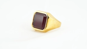 Makro-Detail des Herrenrings mit quadratischem dunkelrotem Edelstein und Gold-Finish