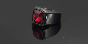 Primer plano de un anillo de hombre en metal negro con una gran piedra roja de corte escalonado