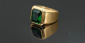 Macro de una gema verde de corte esmeralda en una banda ancha de metal dorado vintage