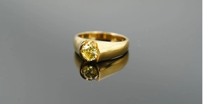 Détail d'une large bague en or avec une grande pierre jaune de taille ronde et reflets