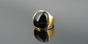 Macro di un anello dorato unisex con una grande pietra nera lucida su sfondo scuro