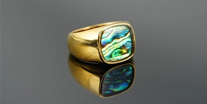 Detail of gold titanium ring with a rectangular abalone shell inlay on reflective surface