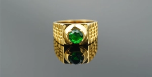 Close-up of men's gold ring with square texture and a round green gemstone