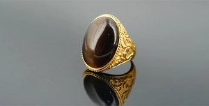 Nahaufnahme von Vintage Titanstahlring mit braunem Katzenaugenstein und Goldgravuren