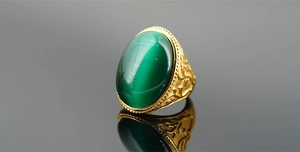 Nahaufnahme eines Vintage-Goldrings mit ovalem grünem Katzenaugenstein und Rankengravur