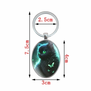 Oval keychain with artistic black cat design, green eyes and butterflies on white background