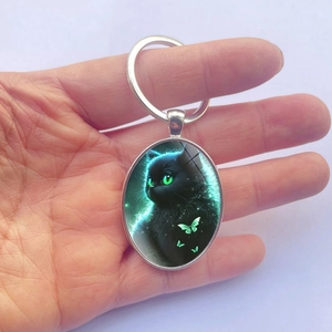 Oval silver metal keychain featuring a cute black cat with green eyes and butterflies