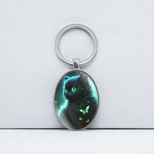 Oval silver keychain featuring a black cat with green eyes and butterfly art pattern
