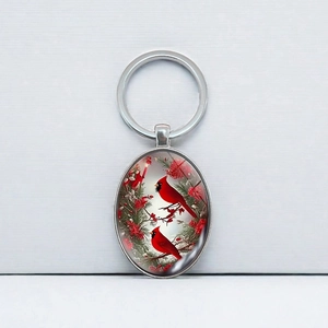 Oval keychain featuring red cardinal birds on pine branches with silver metal ring