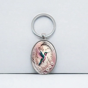 Oval silver hummingbird keychain with embossed colorful bird and white flower detail