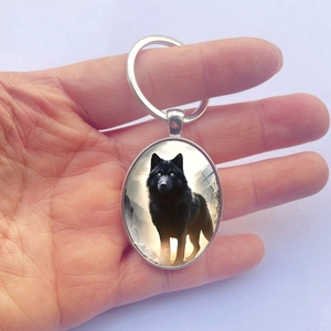 Main tenant un porte-clés ovale en alliage d'argent avec un imprimé d'un loup noir d'art