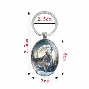 Porte-clés ovale avec loup hurlant à la lune dans une forêt enneigée, longueur de 7,5 cm