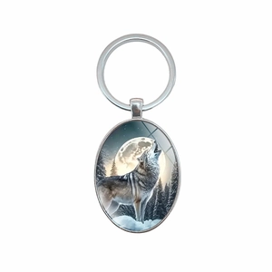Porte-clés ovale avec un loup hurlant sous la pleine lune dans une forêt enneigée