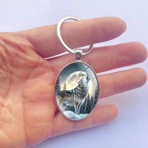 Porte-clés ovale en métal avec un loup hurlant à la pleine lune et forêt enneigée