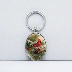 Oval keychain featuring a vibrant Red Northern Cardinal on pine branches with pinecones