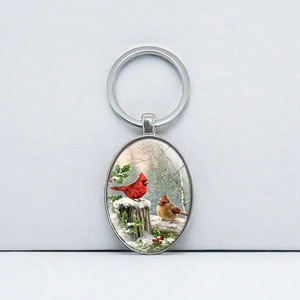 Oval keychain with winter red cardinal birds and green holly design on grey background