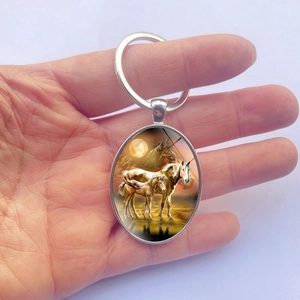Oval silver metal keychain featuring a warm sunset scene with two horses in the center