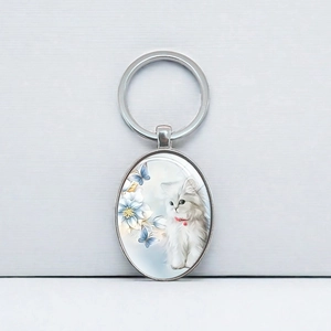 Porte-clés ovale en métal avec chat blanc et fleurs bleues sous cabochon de verre